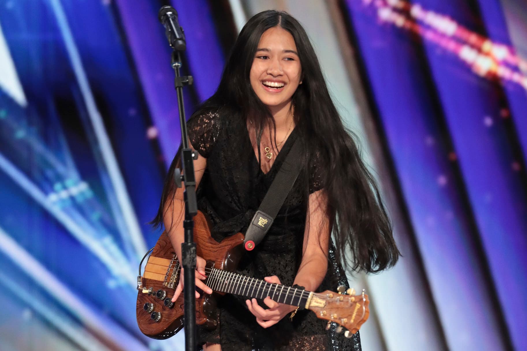 NENE on the AGT stage, smiling in a black lace dress with a wood Ibanez guitar